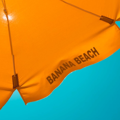 a yellow sun umbrella with banana beach text on the brim